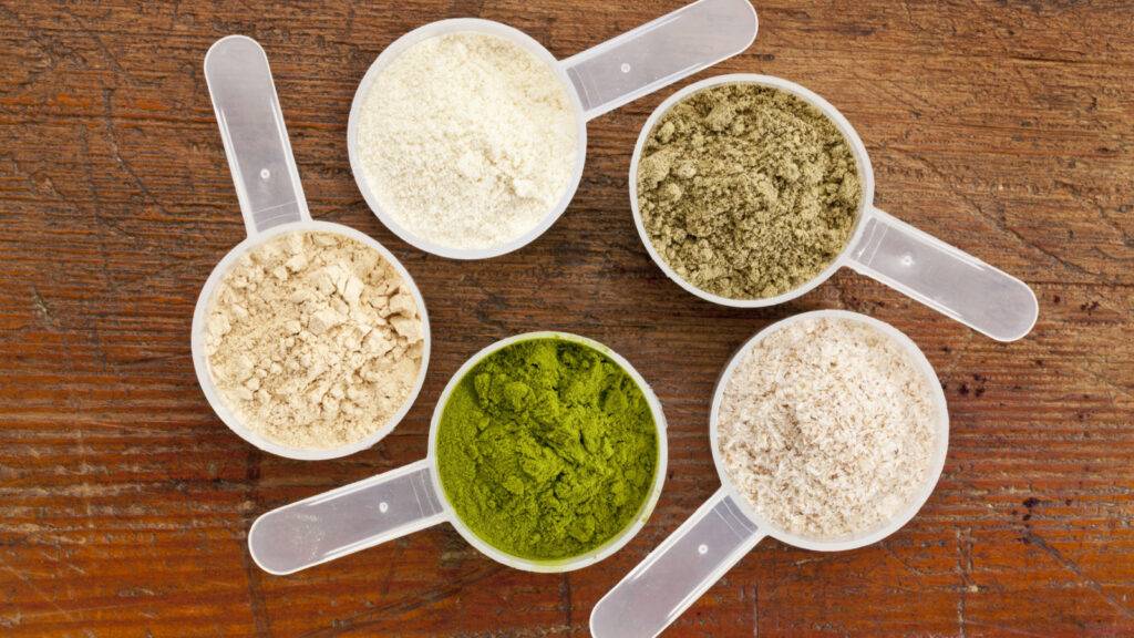 Image displaying various types of protein powder: whey, casein, soy, pea, and hemp, each in a distinct colored powder in clear containers.